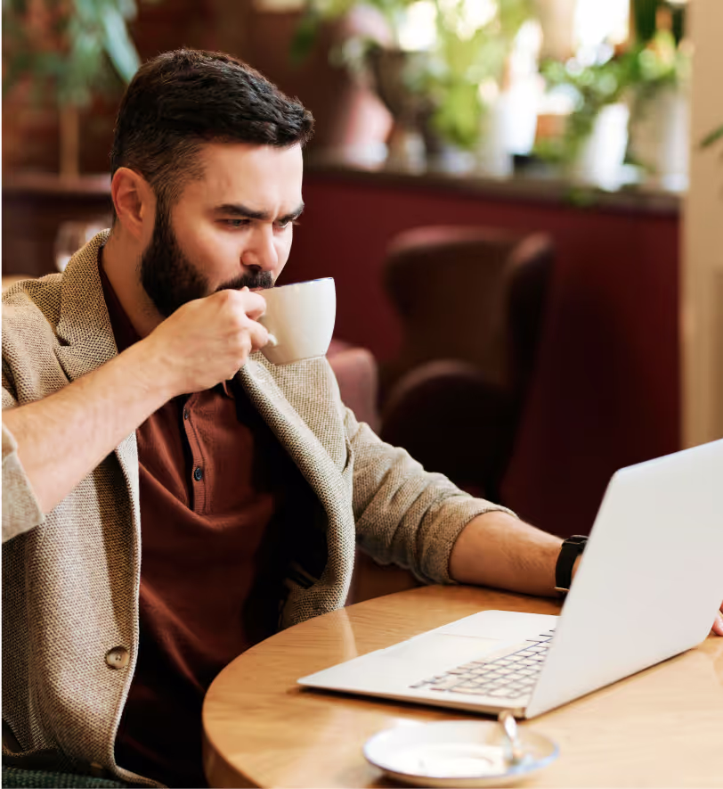 man watching his computer while he drinks coffee
